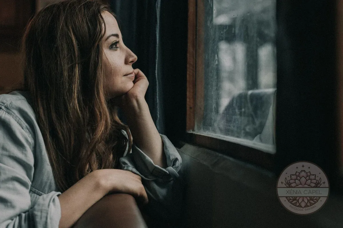 Duelo migratorio: mujer pensativa mirando por la ventana con añoranza de su país de origen