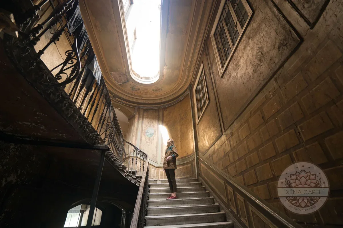 El miedo al fracaso: persona detenida a media escalera mirando hacia la luz, la subida que intimida