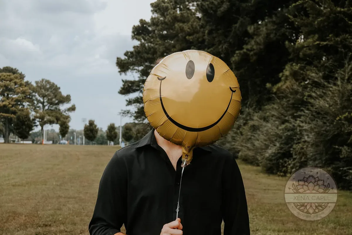 Positividad tóxica: persona ocultando la cara detrás de un globo con una carita sonriente, como una máscara de felicidad forzada
